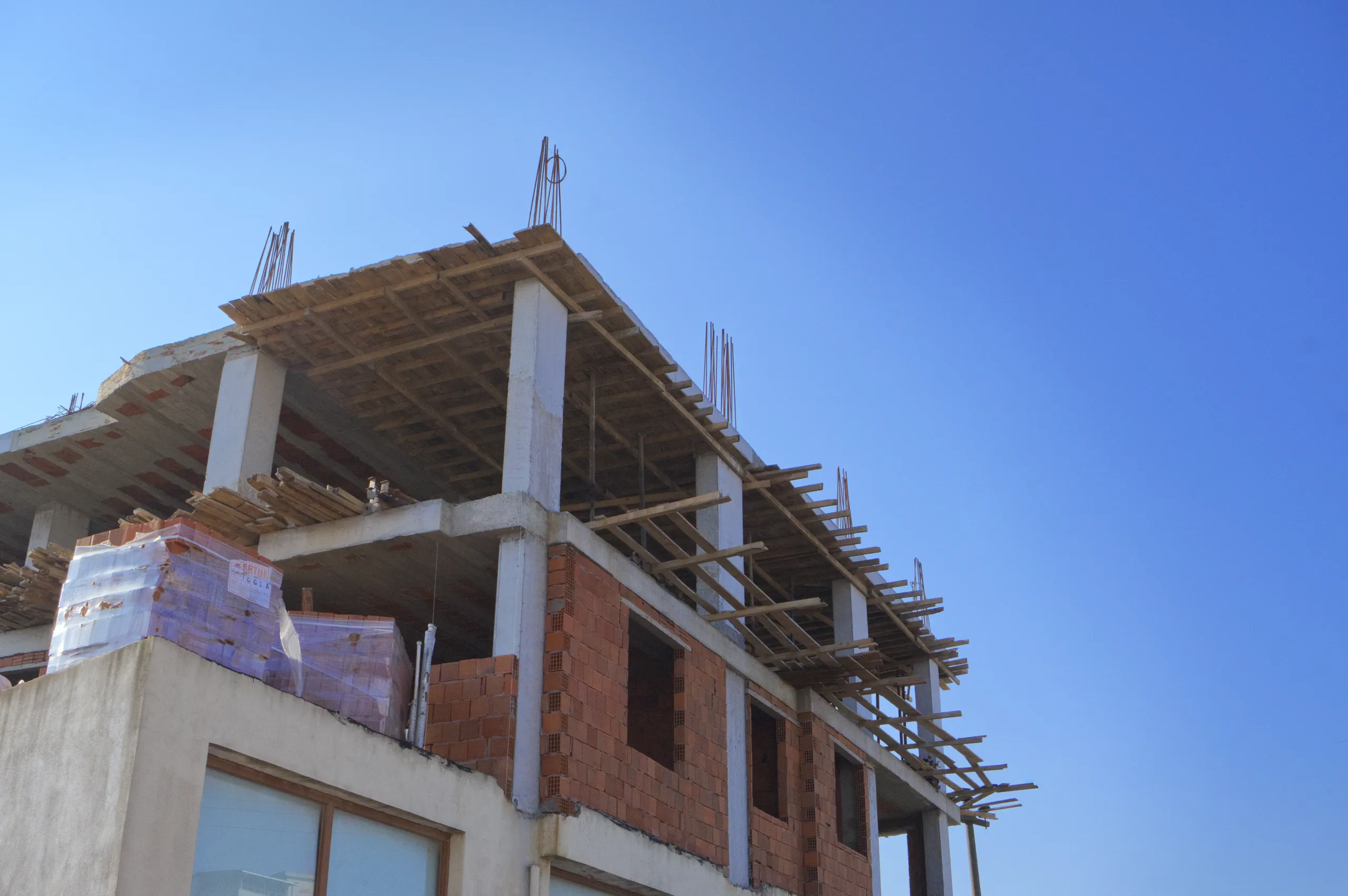 İnşaat sahasında paletler üzerinde streç filmle sarılmış tuğla ve yapı malzemeleri.