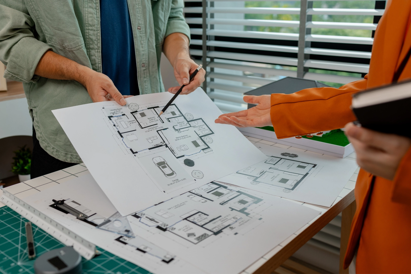 Bir mimar ve müşteri, masa üzerindeki konut kat planlarını inceleyerek tasarım detaylarını tartışıyor.