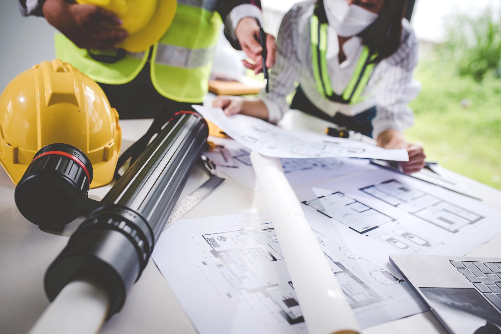 Bir ekip masa üzerindeki mimari planlar ve proje çizimleri üzerinde çalışarak inşaat projesi için stratejik planlama ve uygulama yol haritasını değerlendiriyor.