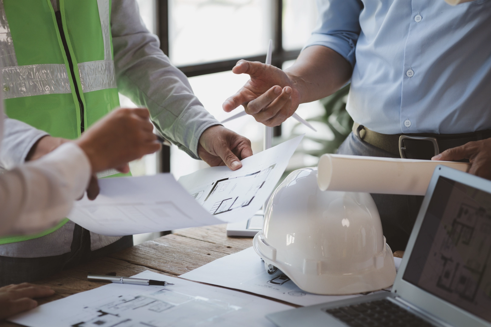 Bir mühendis ve proje ekibi, masa üzerindeki mimari planlar ve proje belgeleri üzerinden inşaat süreci yönetimi ve teknik danışmanlık kapsamında değerlendirme yapıyor.