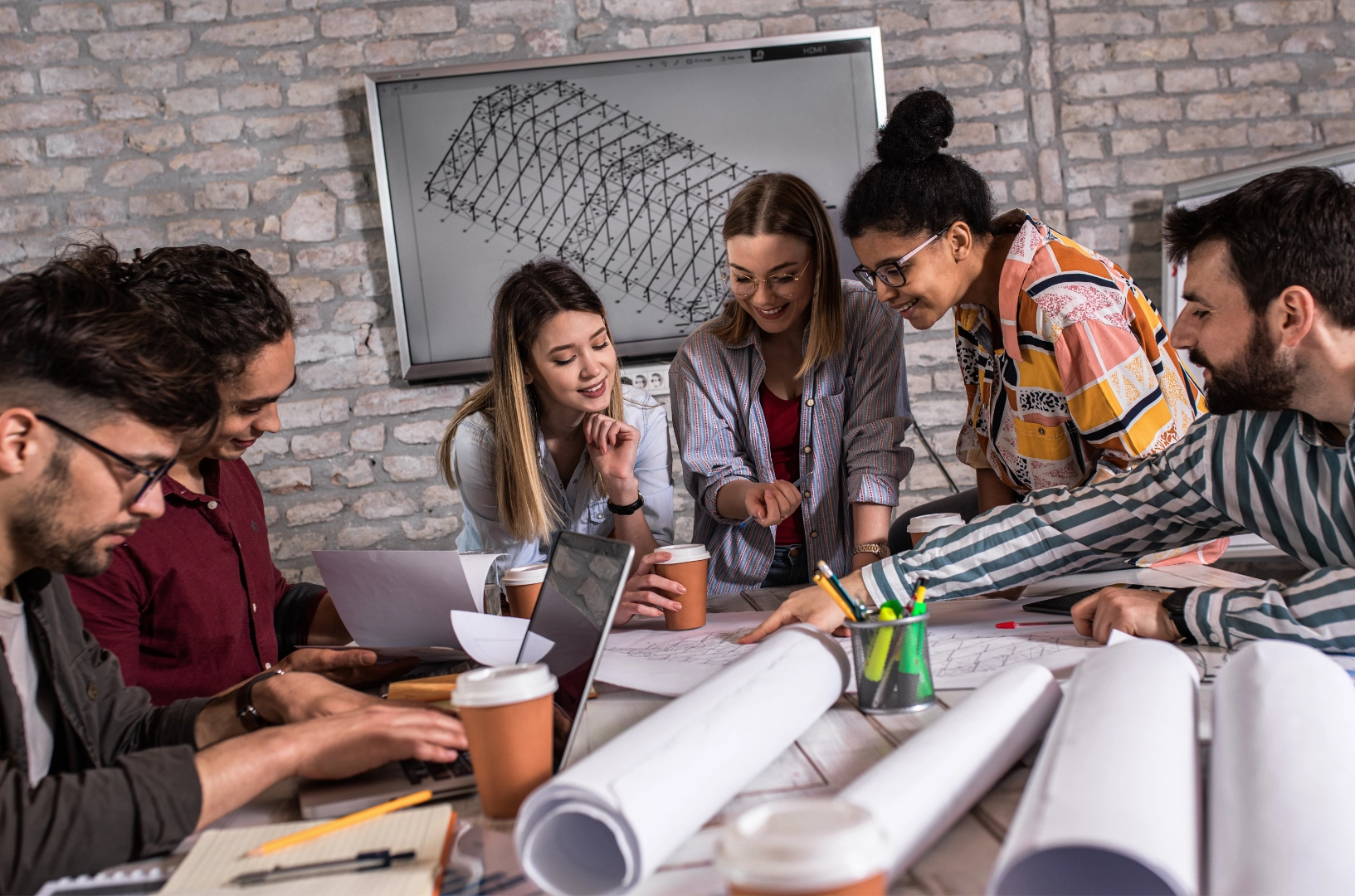 Bir masa etrafında toplanmış mimar ve tasarım ekibi, proje çizimlerini inceleyip planlar üzerinde birlikte çalışıyor.