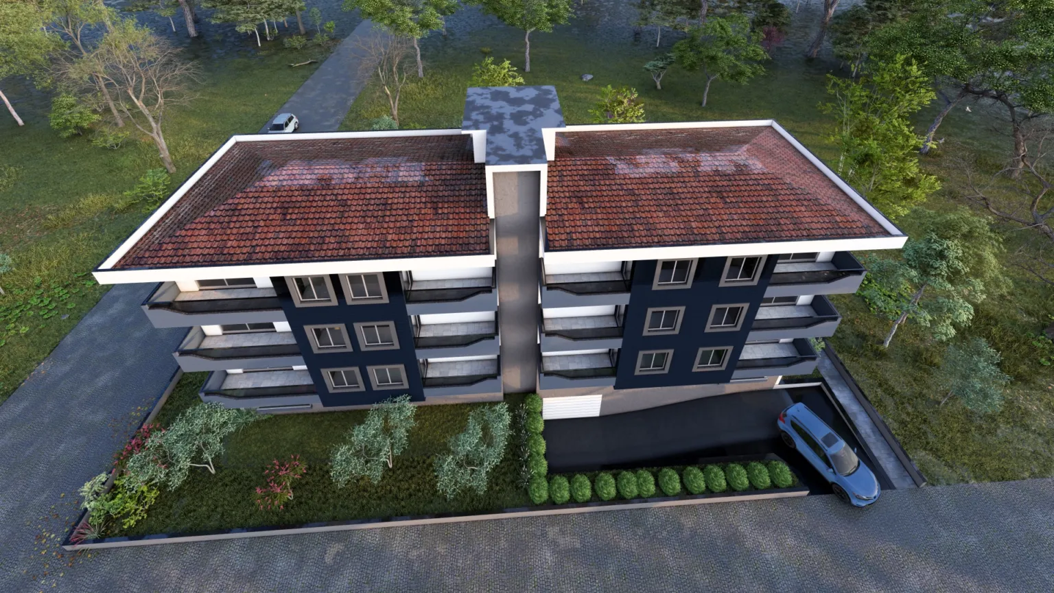 Top aerial view of a modern residential building highlighting the twin red tiled roofs, central structural core, balconies, landscaped garden, and driveway.
