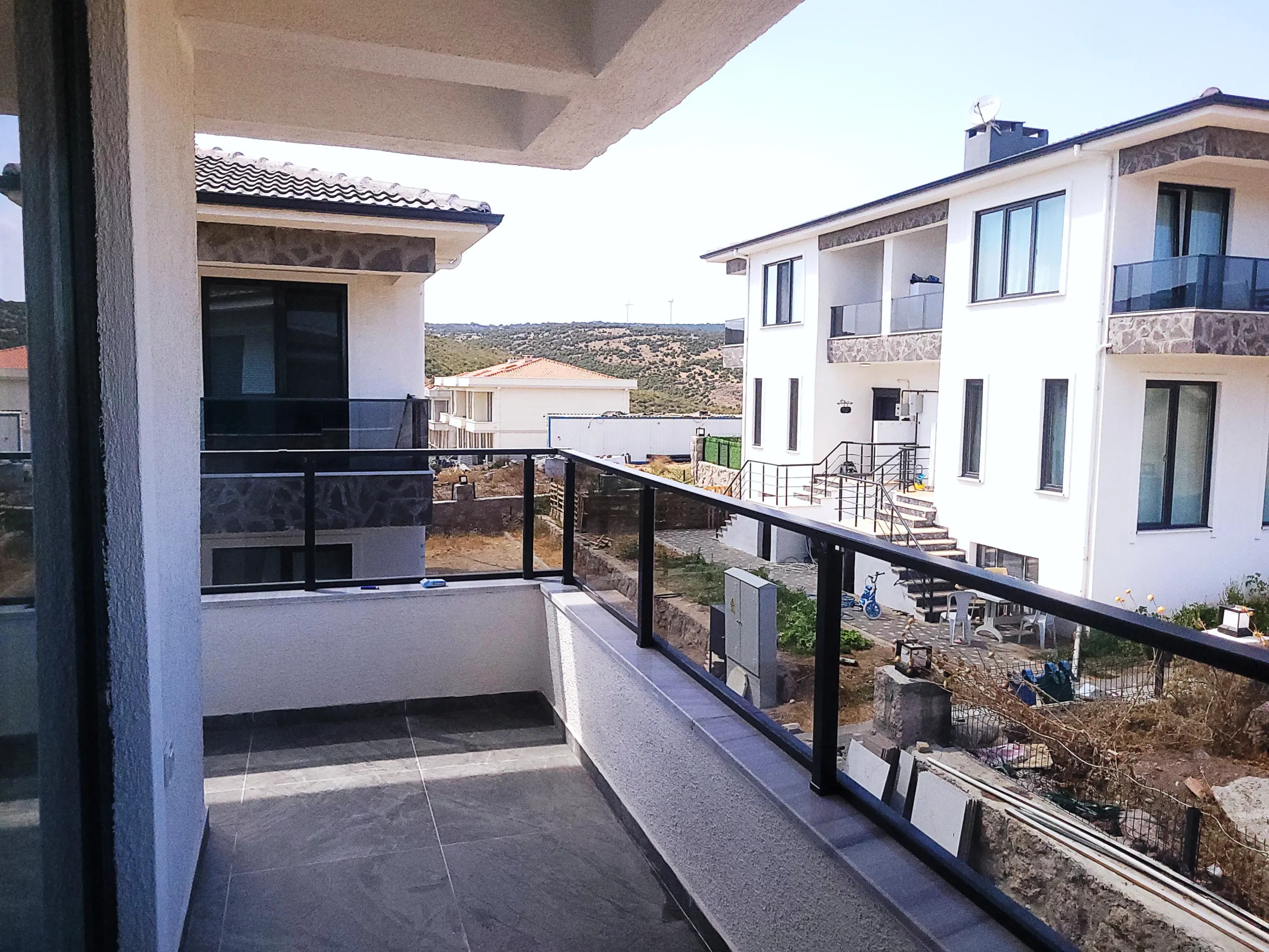 White residential buildings and surrounding hills viewed from a balcony with glass railings.