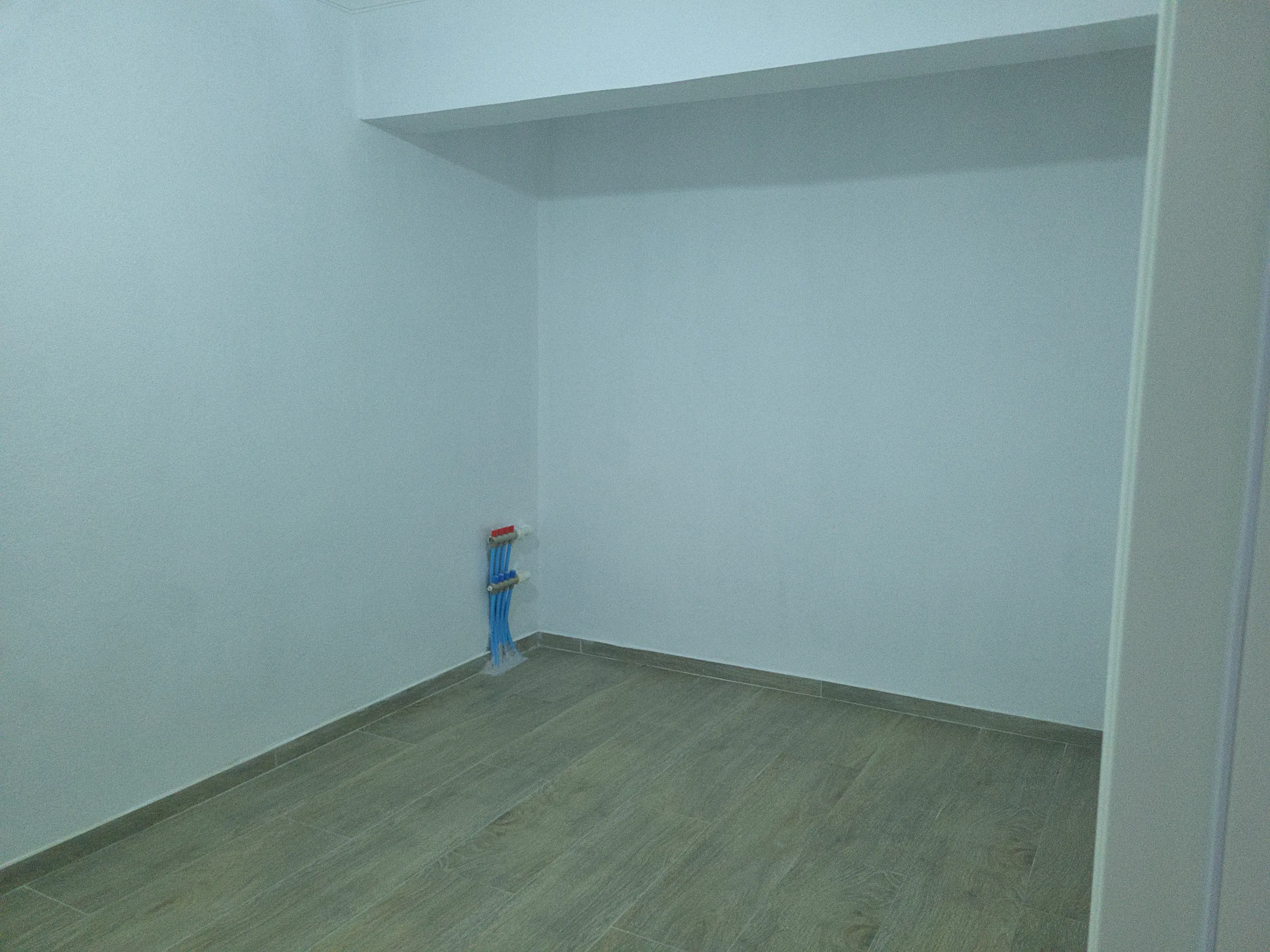 Empty kitchen area with grey flooring, white walls, and prepared plumbing connections.
