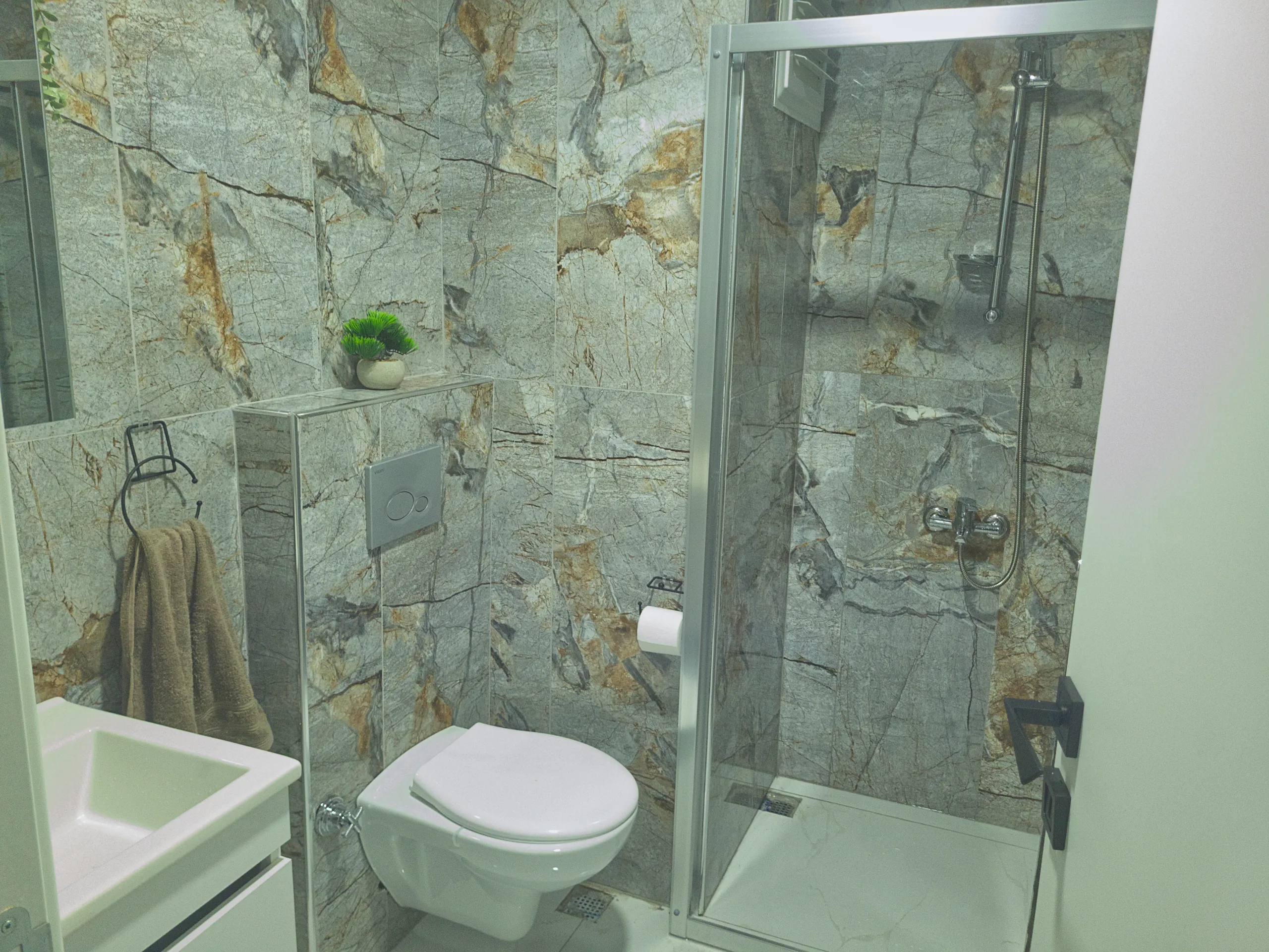 Modern bathroom with marble-patterned walls, a glass shower enclosure, and a wall-mounted toilet.
