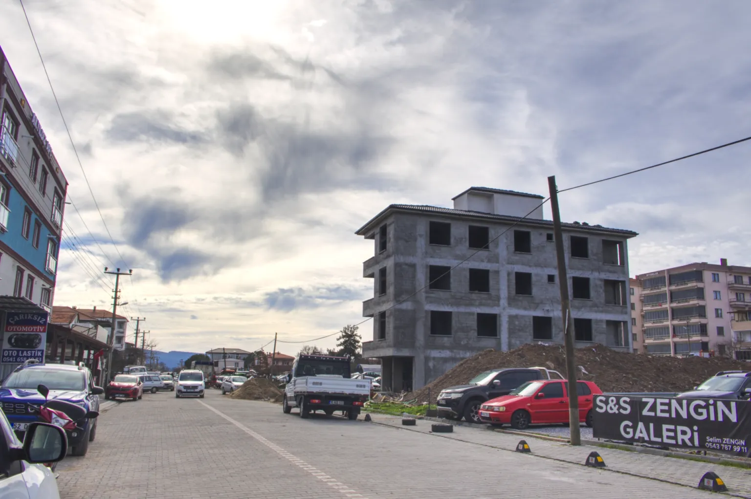 Ayvacık’taki Small House projesinin işlek bir cadde üzerindeki betonarme inşaatını ve çevredeki araçları gösteren sokak görünümü.