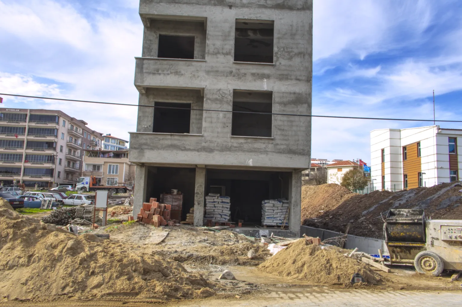 Small House construction site with sand piles, bricks, cement bags and the unfinished concrete building in the background.