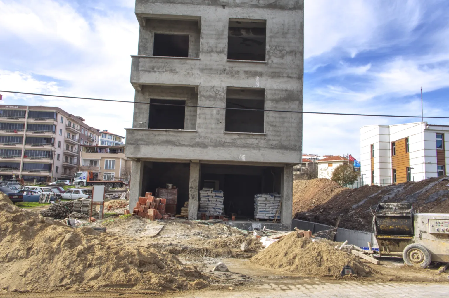 Small House projesinin zemin katındaki geniş açıklıkları, üst katlardaki pencere boşluklarını ve şantiye malzemelerini gösteren cephe fotoğrafı.