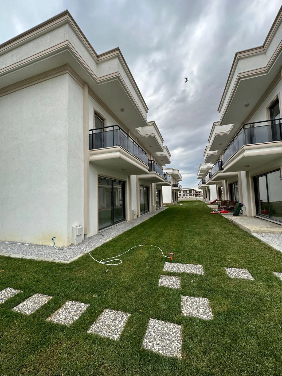 White duplex homes lining a green courtyard with a stone walkway at Gelibolu Beyaz Kent.