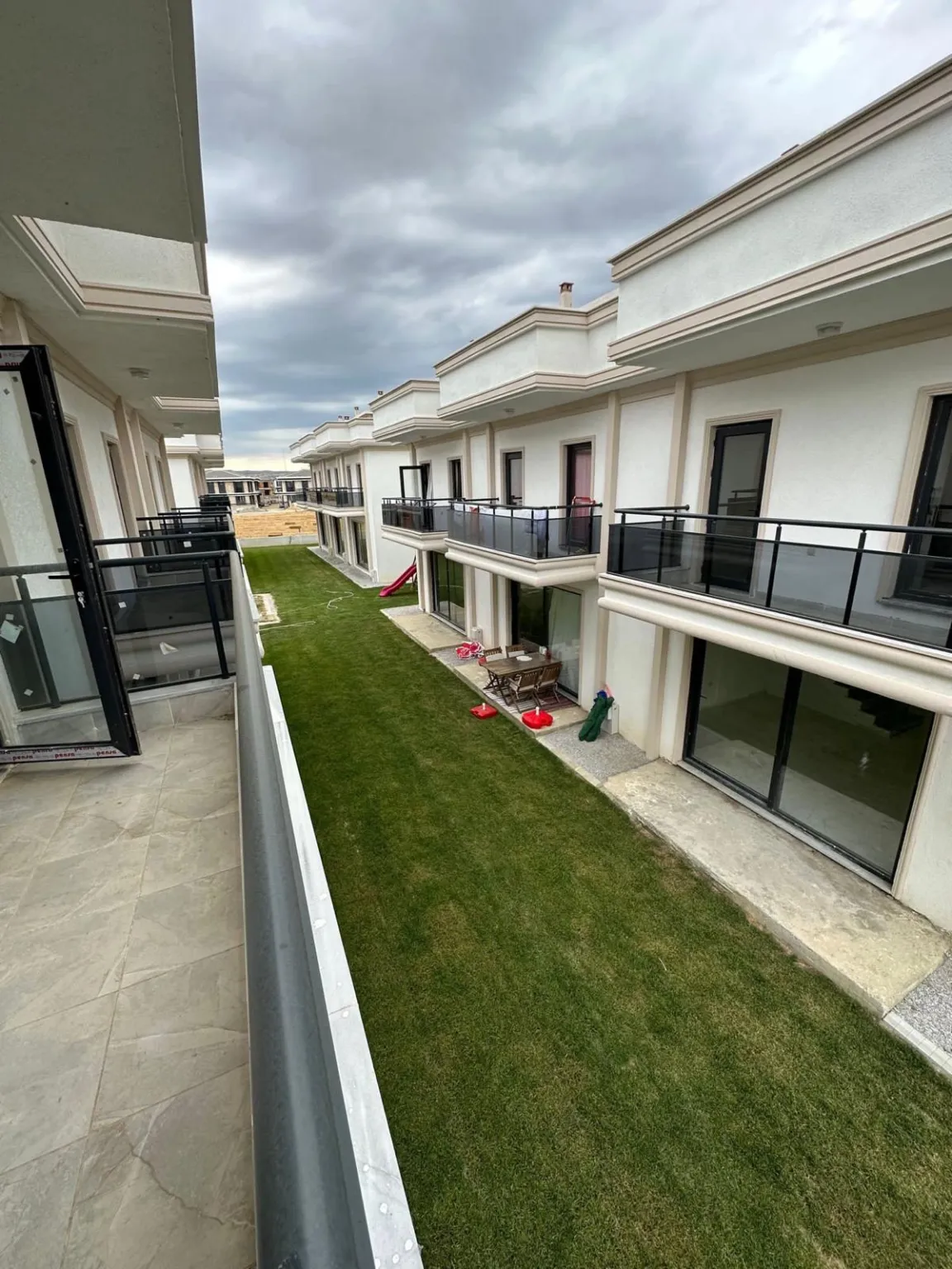 Siyah balkon korkulukları, beyaz dubleks konutlar ve ortak çim alanın üst kattan görünümü.