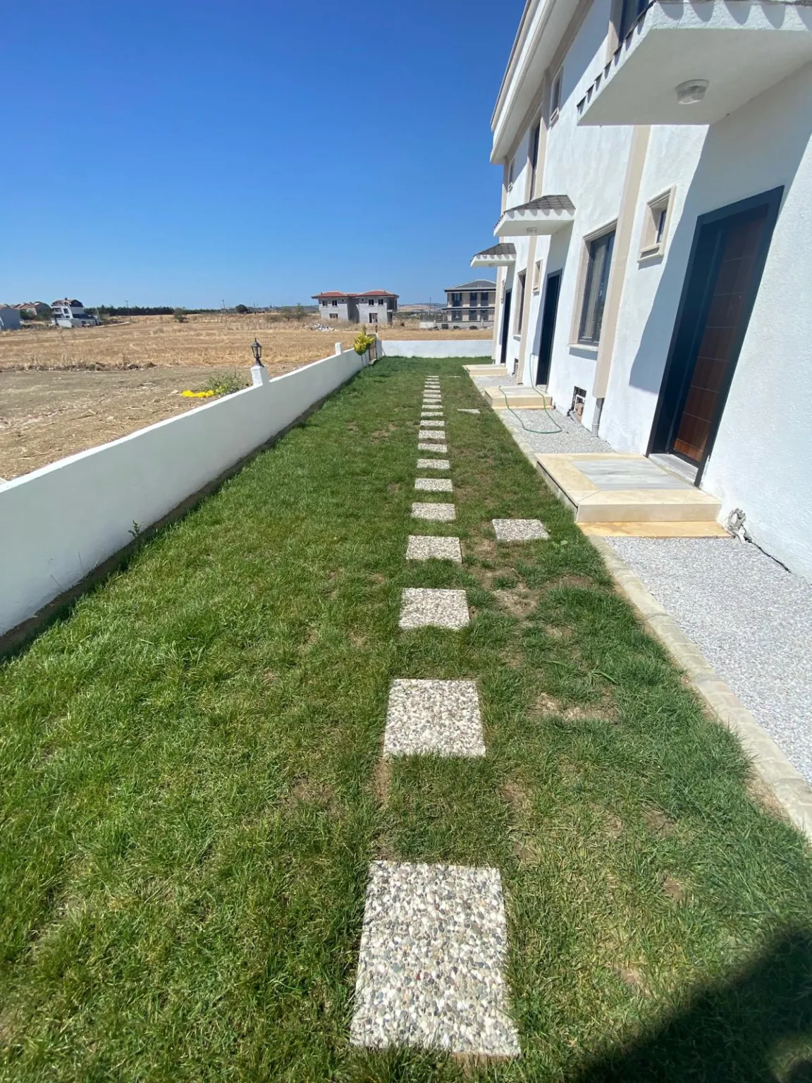 Lawn and stepping-stone path beside a white home, with open land in the background.