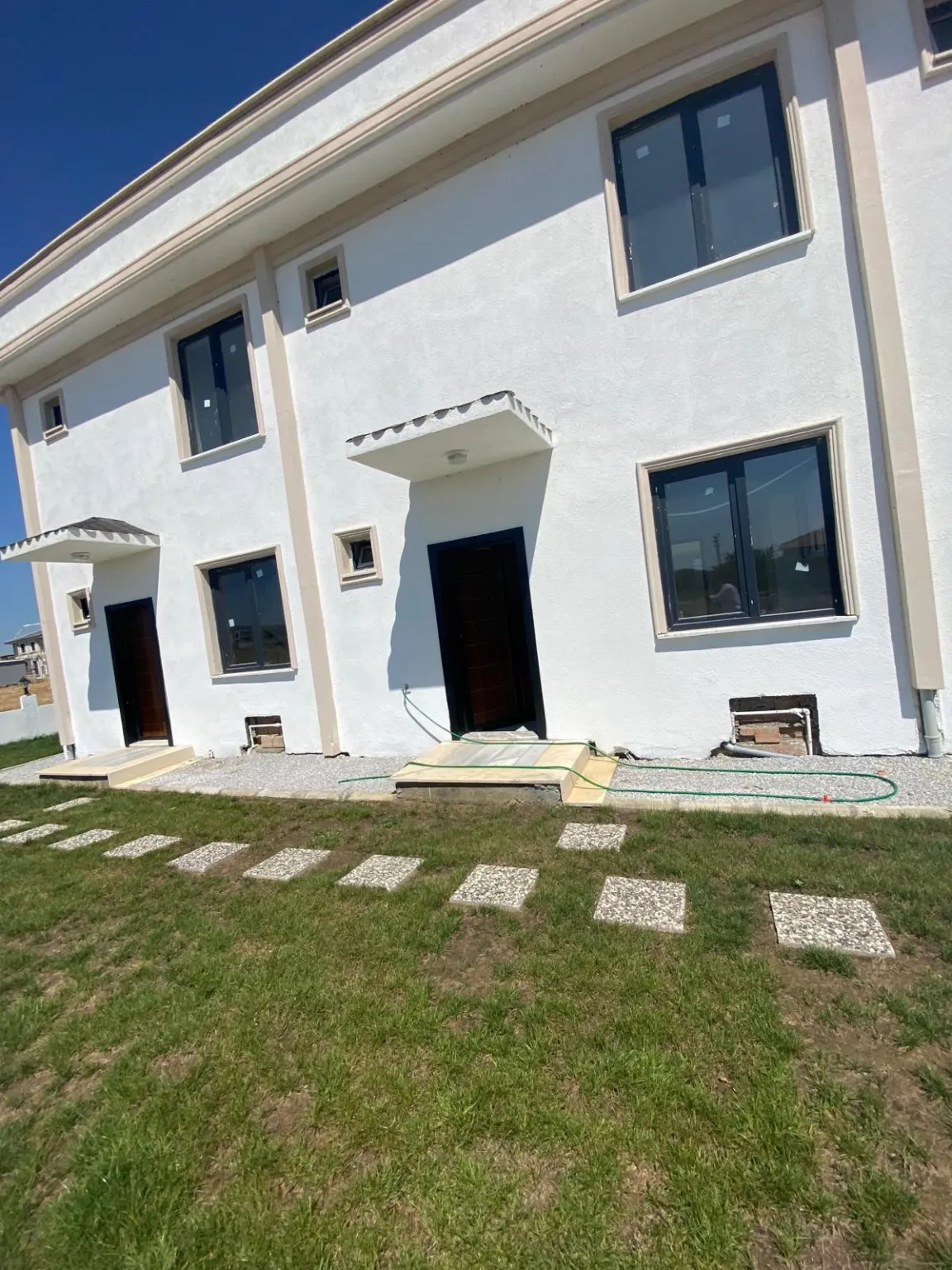 Bahçeye açılan kapı ve pencereleriyle iki katlı beyaz dubleks konutun arka cephesi.