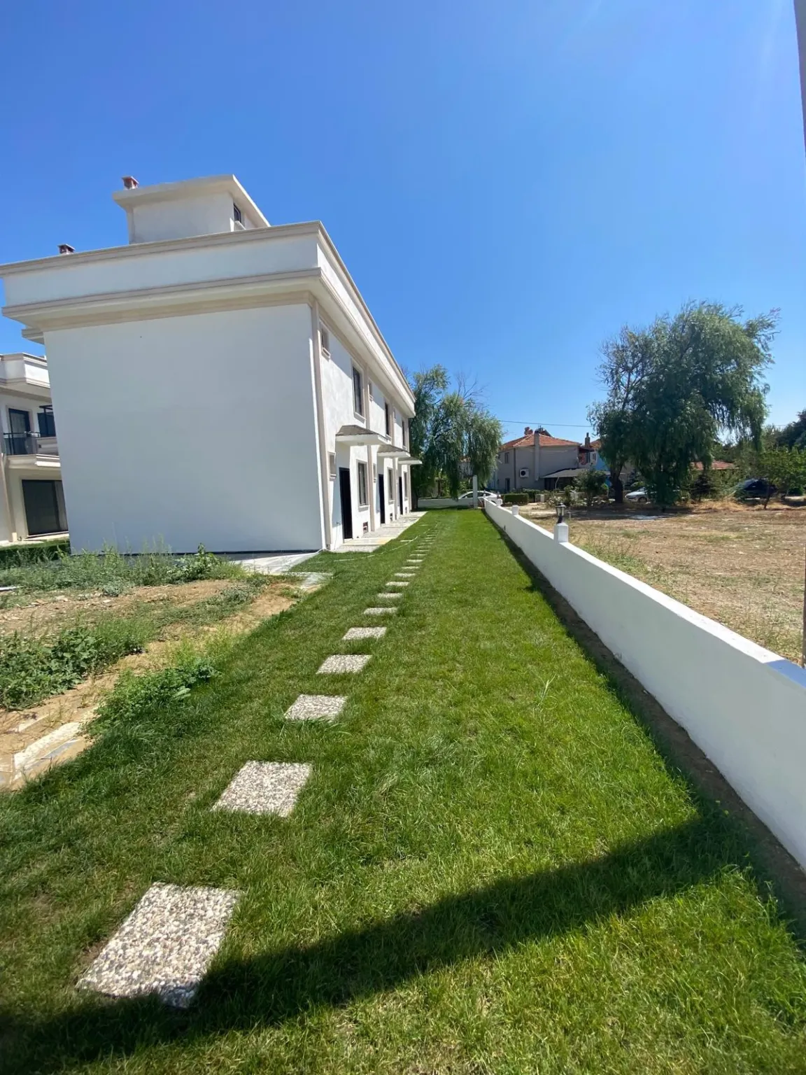 Lawn and stepping-stone walkway extending alongside a white residential block.