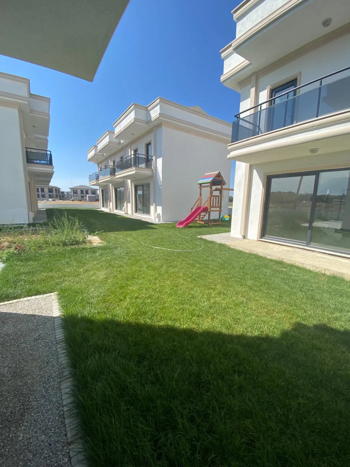 Beyaz dubleks konutlarla çevrili yeşil ortak bahçe ve arka plandaki çocuk oyun alanı.