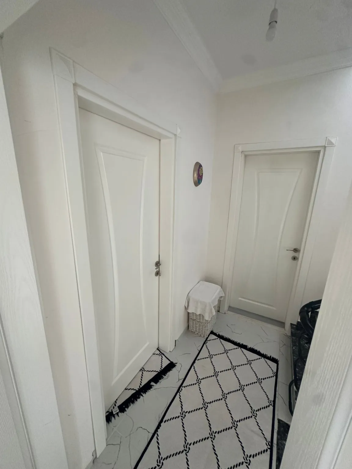 Hallway with white interior doors, marble-patterned flooring, and black-and-white runner rugs.