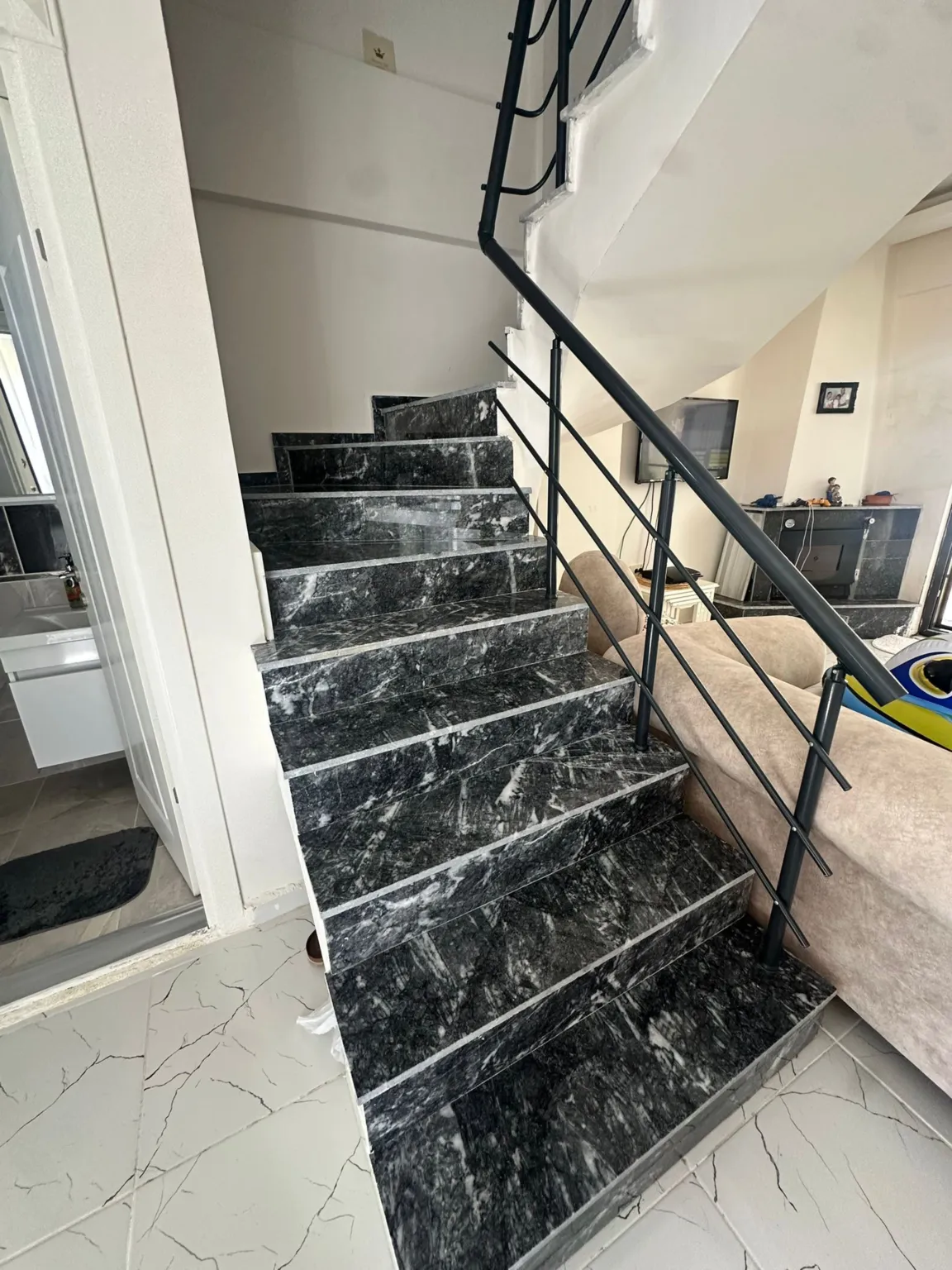 Interior duplex staircase with black marble steps and black metal railings.