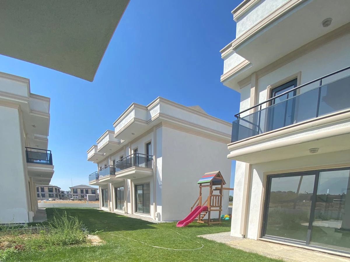 Gelibolu Beyaz Kent Sitesi’ndeki siyah cam balkonlu, iki katlı beyaz konutlar ile yeşil ortak alanda bulunan çocuk oyun parkı.