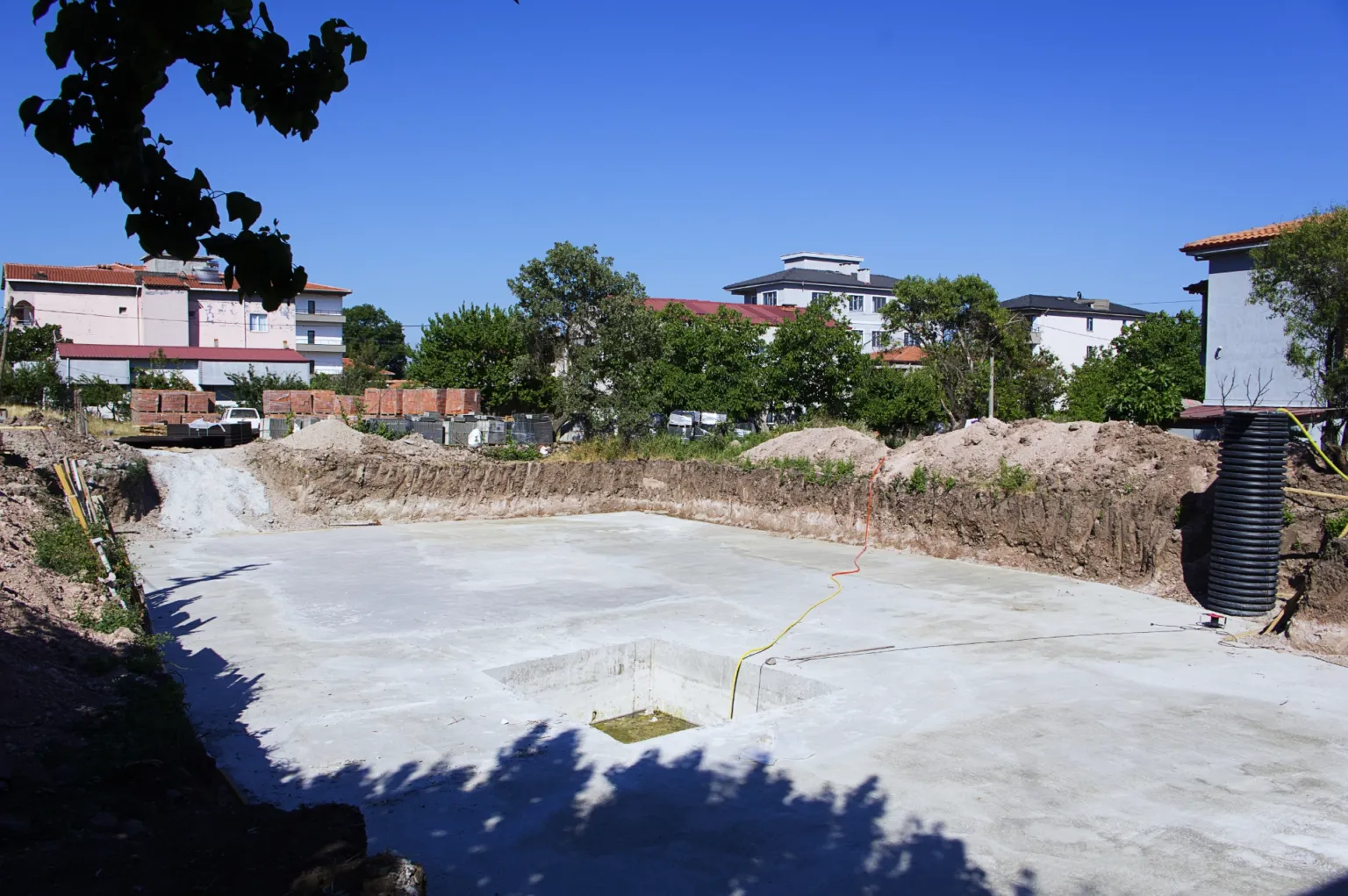 Kazı alanında tamamlanan beton temel tabanı, ortasındaki boşluk ve kenarında bulunan siyah drenaj borusuyla birlikte şantiye görünümü.