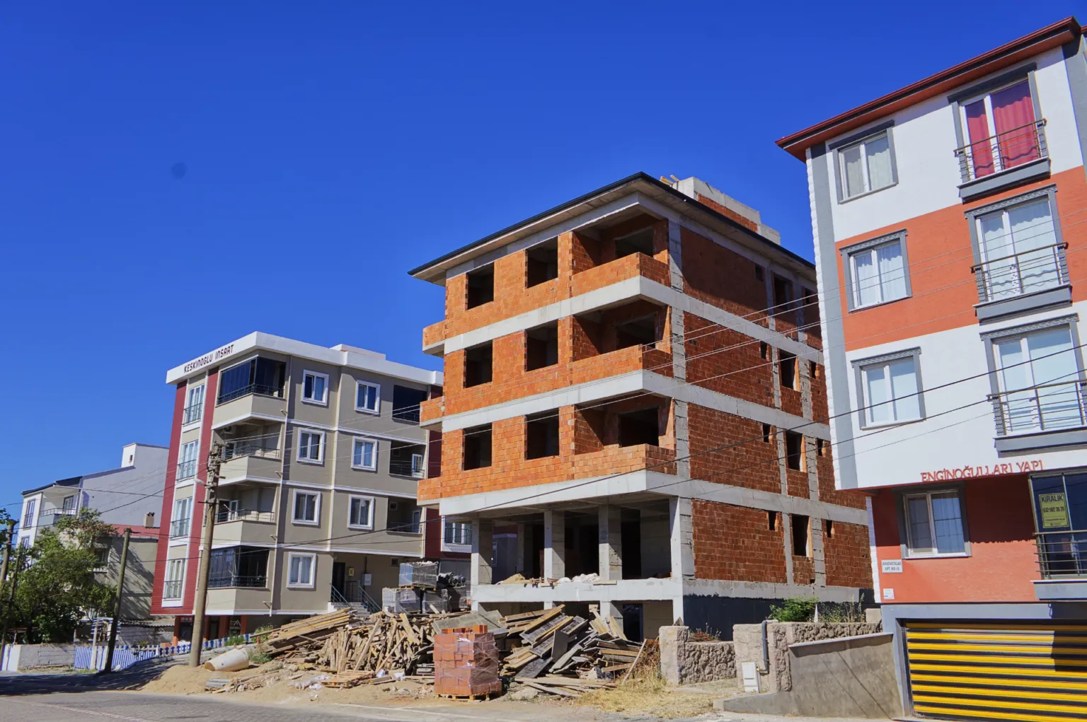 Construction-site view of Ezine Apartment with its reinforced-concrete structure and brick infill walls nearing completion, with building materials in front.