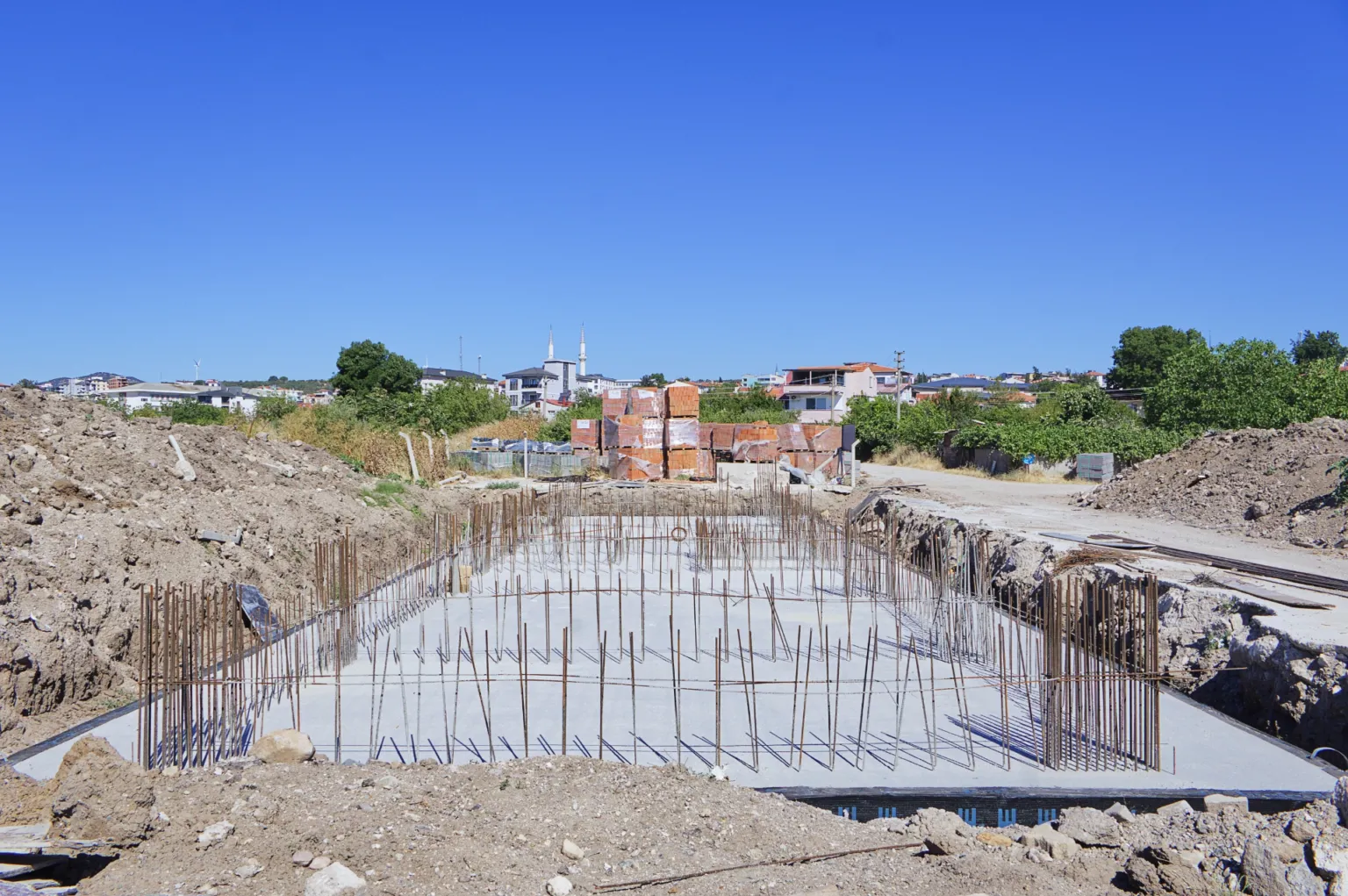 Front view of the construction site showing the concrete foundation base, surrounding vertical reinforcement, and excavation area.