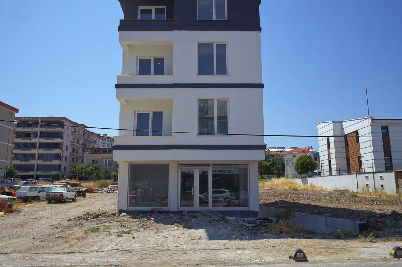 Front construction view of the Small House project showing its white and dark grey façade, balconies and large glazed ground-floor space.
