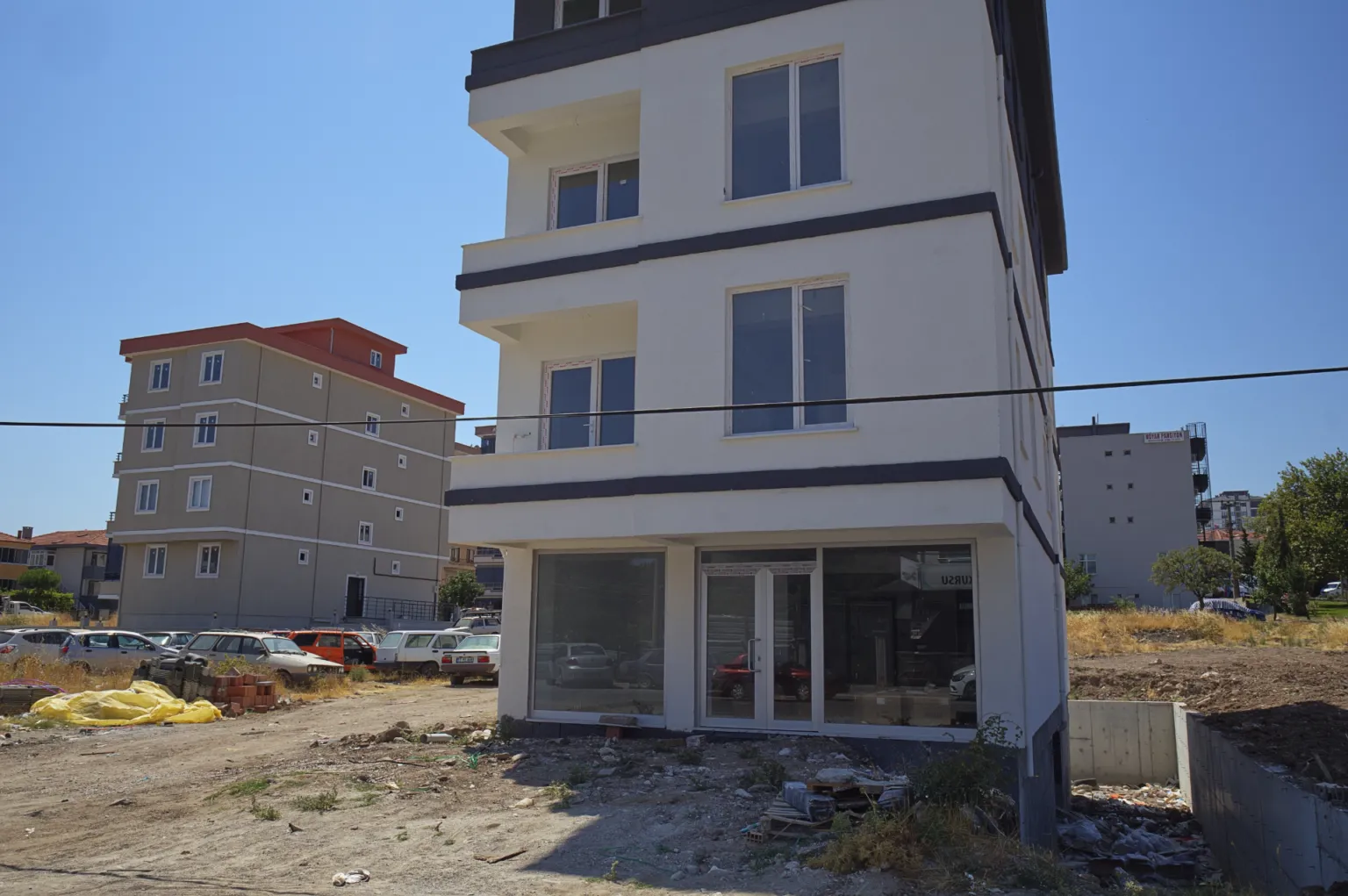 View of the Small House project’s white façade with dark grey horizontal details, large storefront windows and ongoing site work.