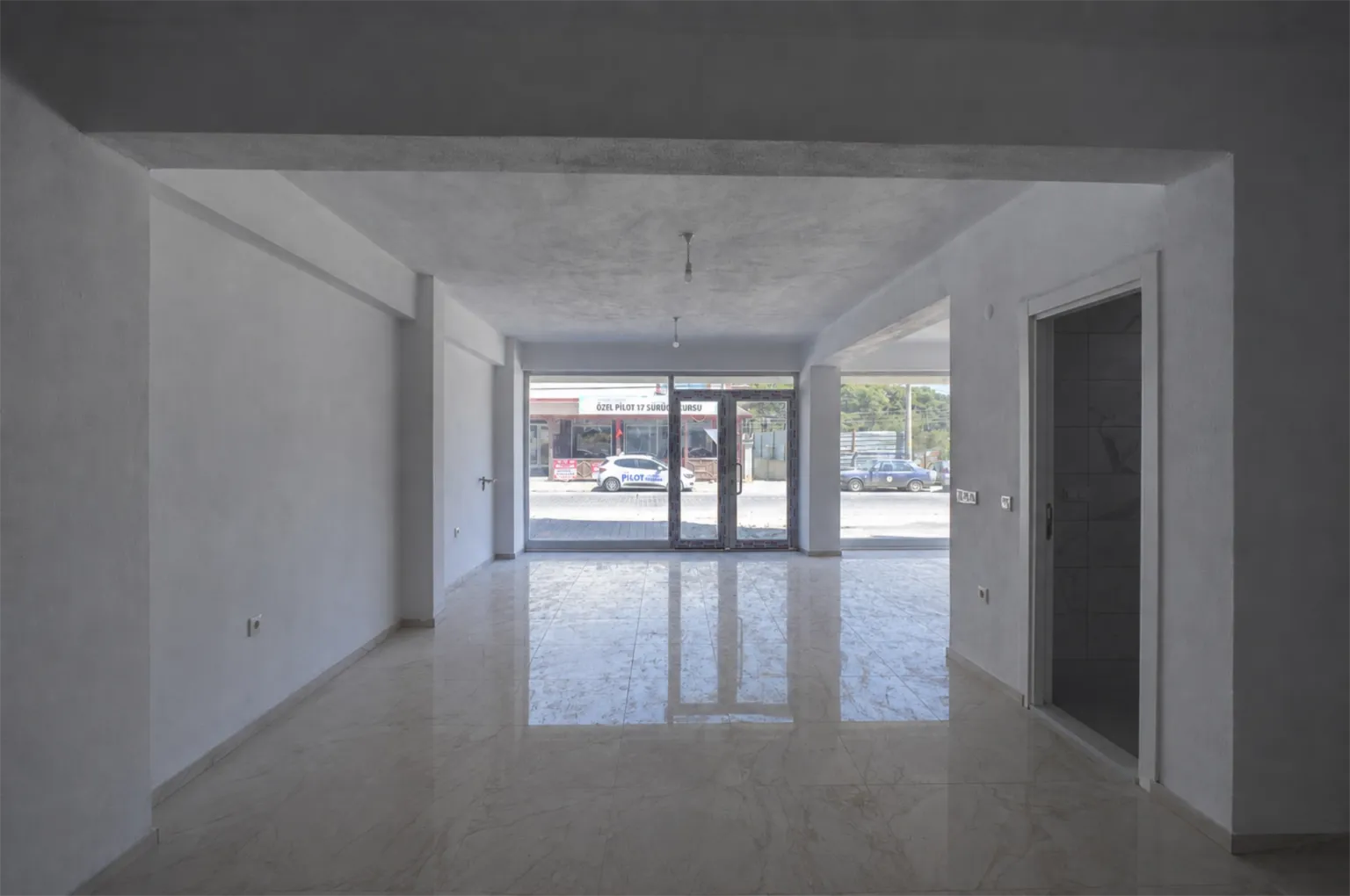 Empty ground-floor commercial space in the Small House project, featuring glossy marble-look flooring and wide glass storefronts facing the street.