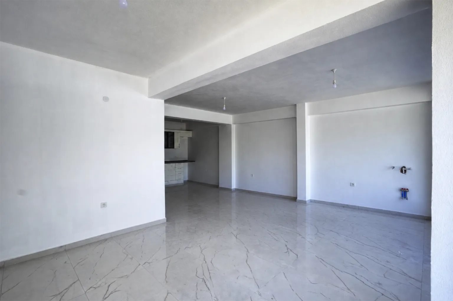Small House projesinde beyaz duvarlara, parlak mermer görünümlü zemine ve arka bölümde açık mutfağa sahip geniş yaşam alanı.