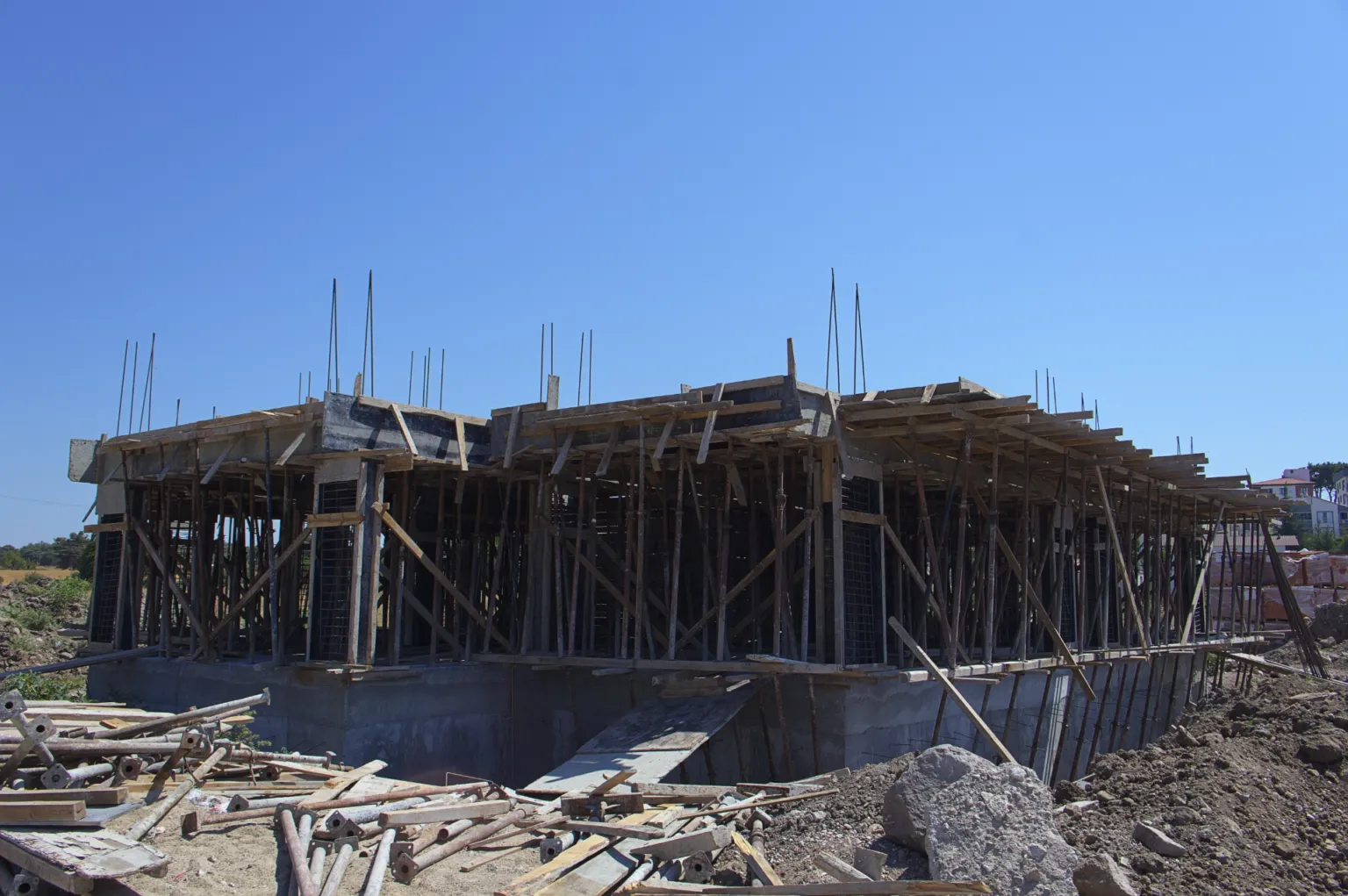 Reinforced-concrete building under construction with slab formwork supported by timber props and rising column reinforcement.