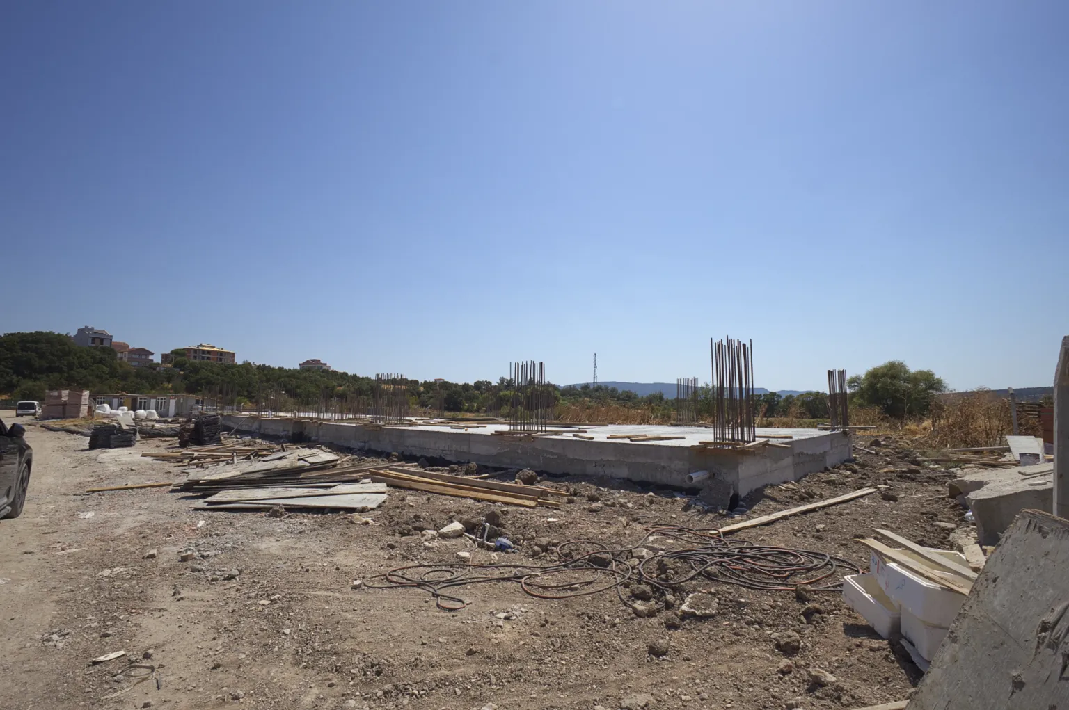 Wide construction-site view showing concrete foundation walls, column reinforcement, and formwork and steel materials spread across the area.