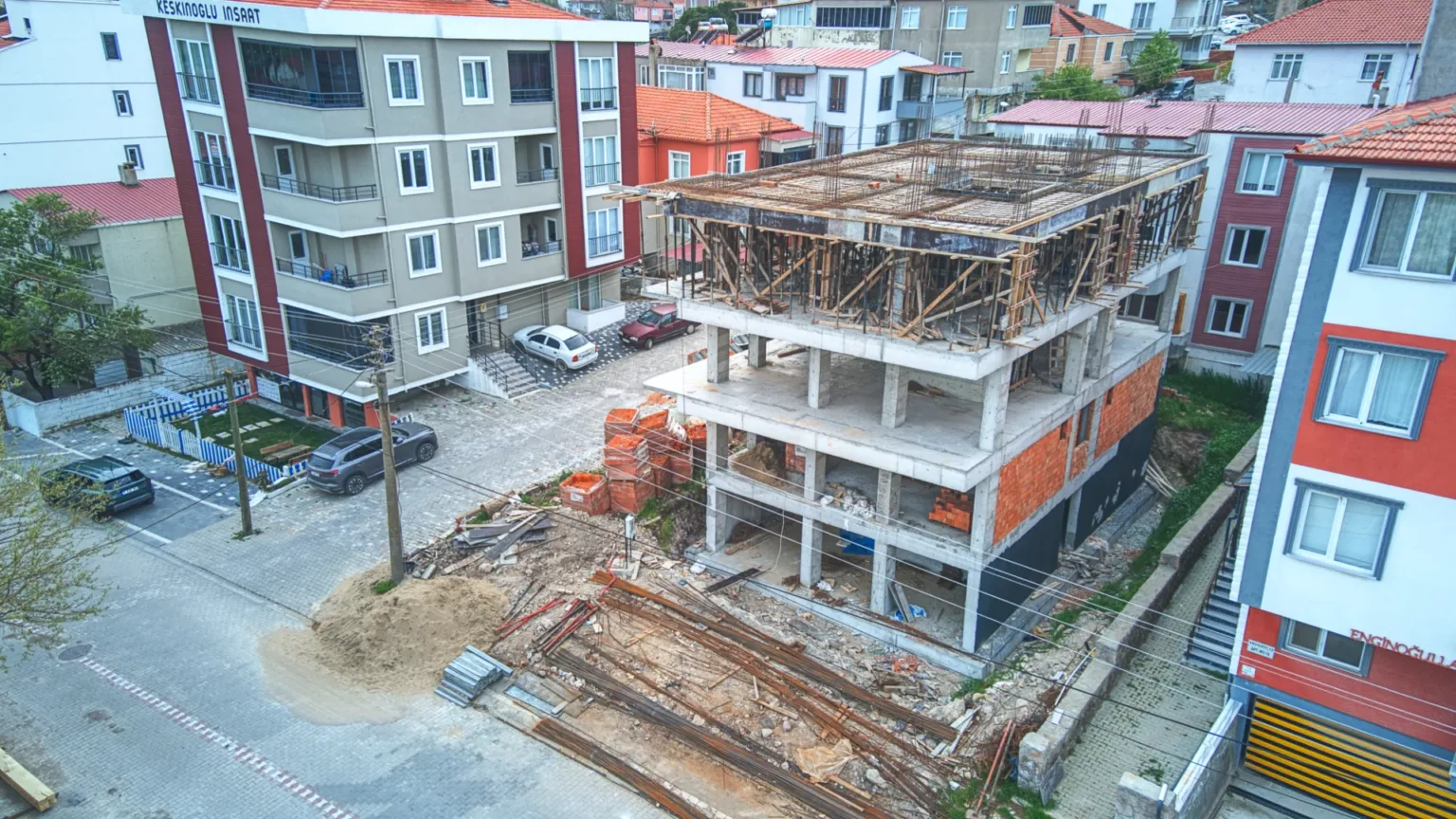 Aerial construction photo of Ezine Apartment showing its reinforced-concrete structure, brick walls, and timber formwork on the upper floor.