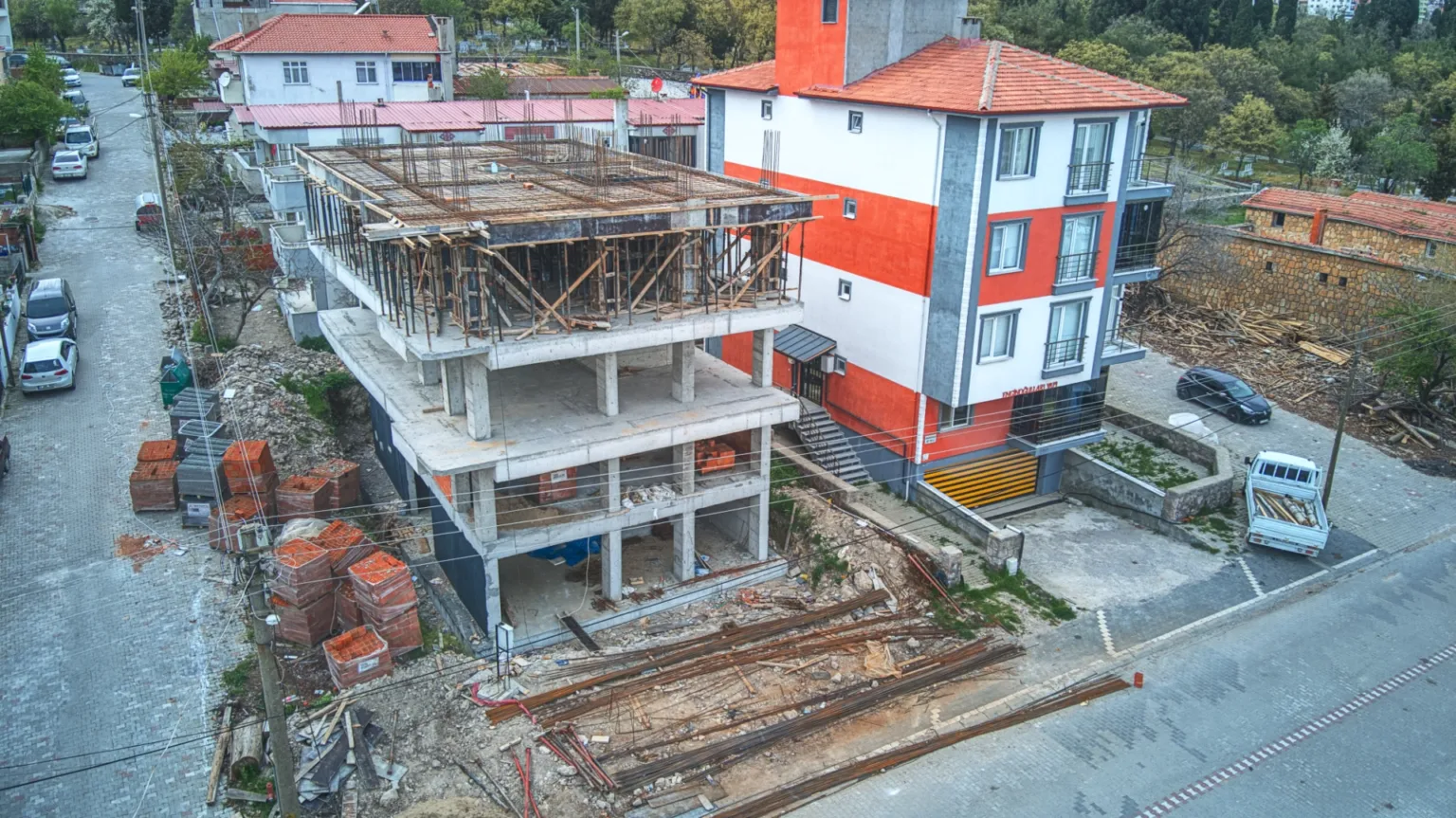 Ezine Apartmanı’nın betonarme katlarını, üst kat kalıplarını ve bitişiğindeki konut yapılarını gösteren çapraz açılı hava fotoğrafı.
