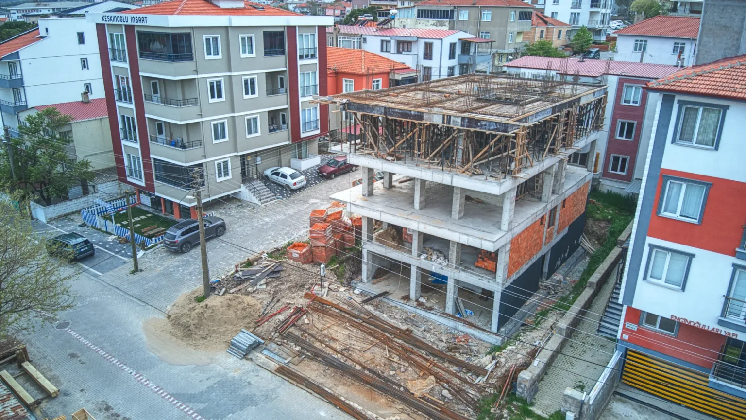 Ezine Apartmanı’nın devam eden kaba inşaatını, çevresindeki apartmanları ve cadde üzerindeki şantiye alanını gösteren geniş açılı hava fotoğrafı.