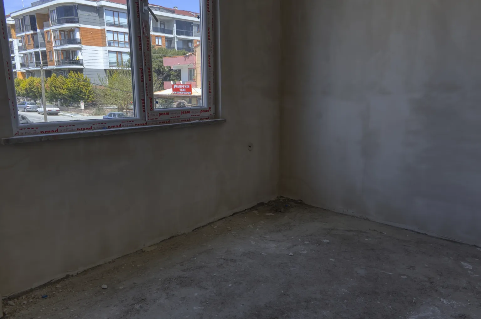 Small House projesinde yapımı devam eden boş bir odanın penceresinden görünen çevredeki apartmanlar ve cadde.