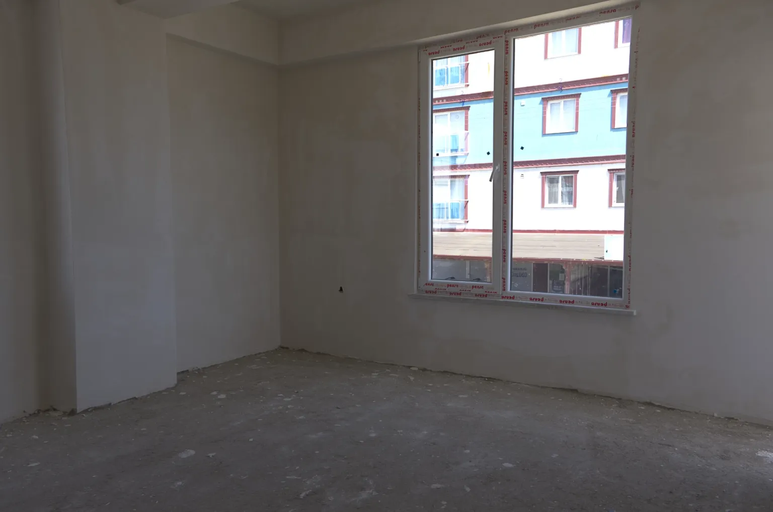 Unfinished empty room in the Small House project with a large window, plastered walls and a raw concrete floor.