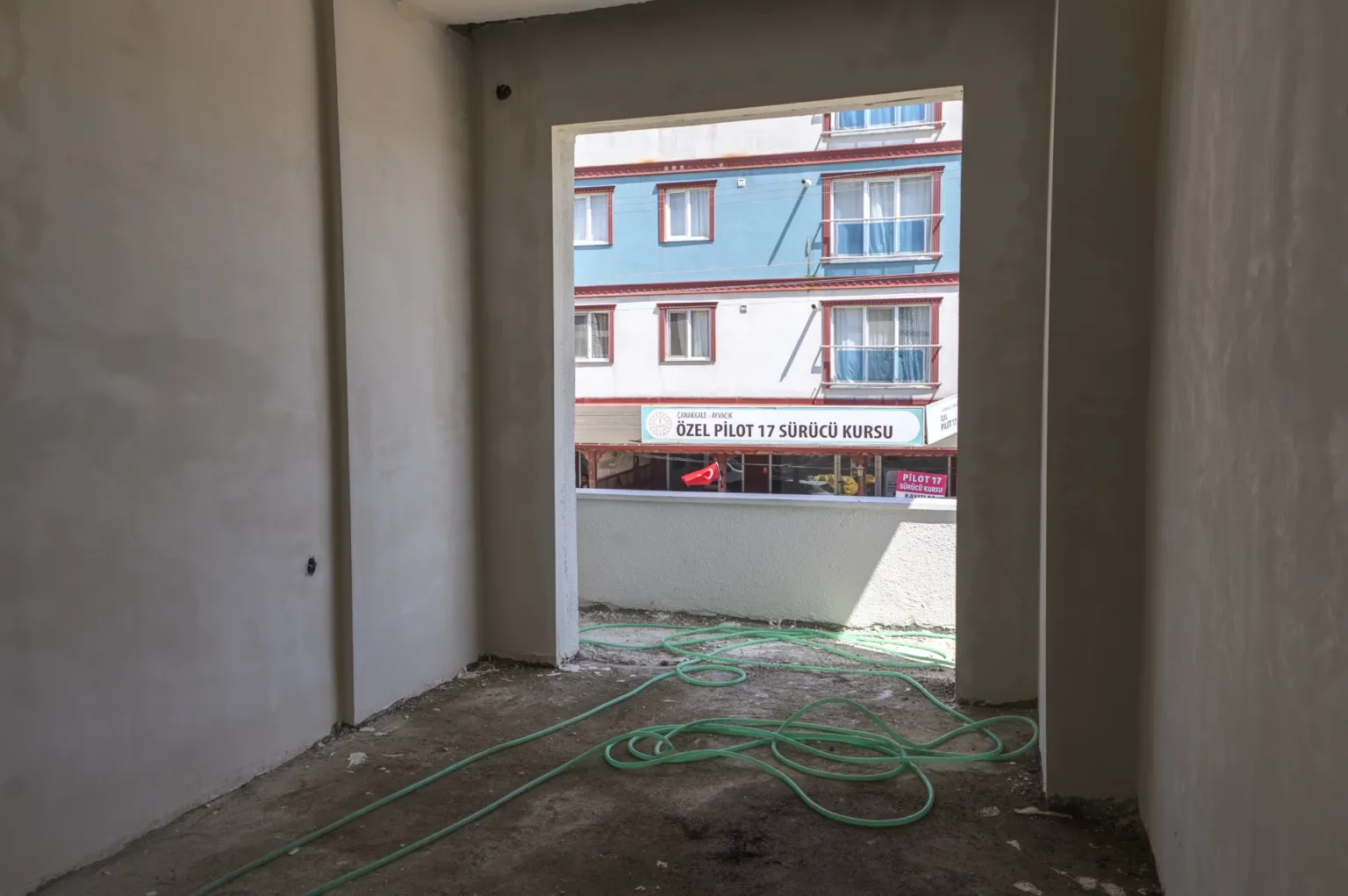 Unfinished room in the Small House project with a wide balcony opening and green hoses spread across the concrete floor.
