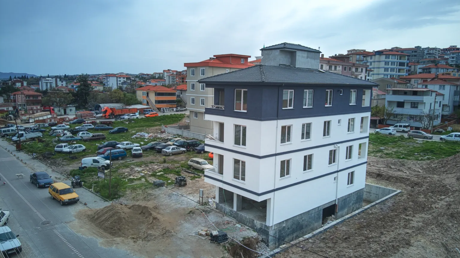Aerial view of the Small House project’s white and dark grey exterior, tiled roof and surrounding construction site.