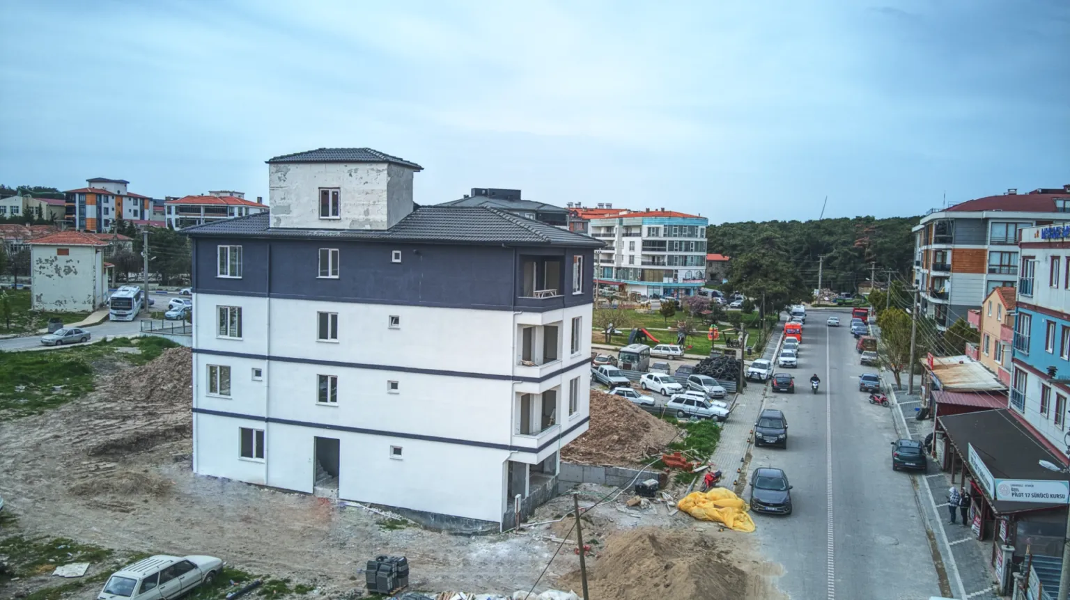 Small House projesinin beyaz yan cephesini, koyu gri üst katını, balkonlarını ve bitişiğindeki caddeyi gösteren havadan görünüm.