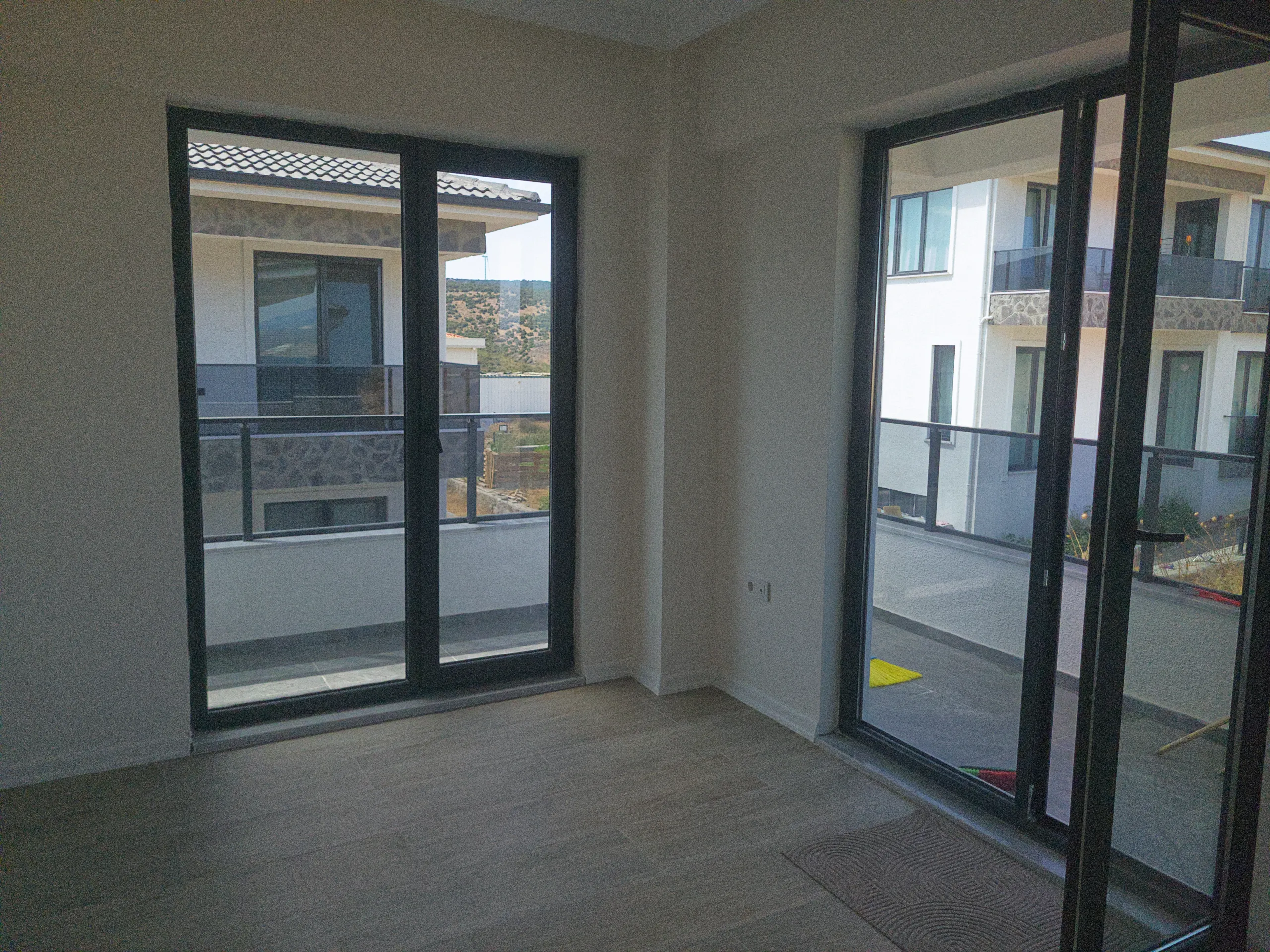 Geniş cam kapılarla çevrelenen, balkona ve site içerisindeki konutlara bakan aydınlık oda.